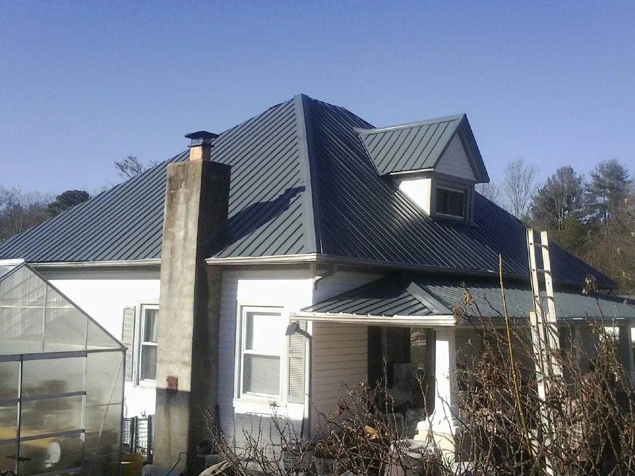 Dark blue standing seam metal roof on a white farmhouse with dormer — Slate & Tile Roof Repair by Roofing Brothers in Hayesville