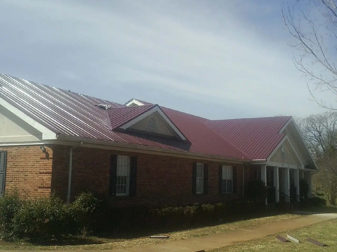 Red metal roof with gabled entries on a long brick building, from a Hail Damage Roof Repair job in Hayesville