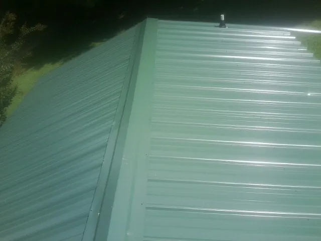 New green metal panels meeting at the ridge of a roof — Flat Roof Repair work by our crew in Hayesville