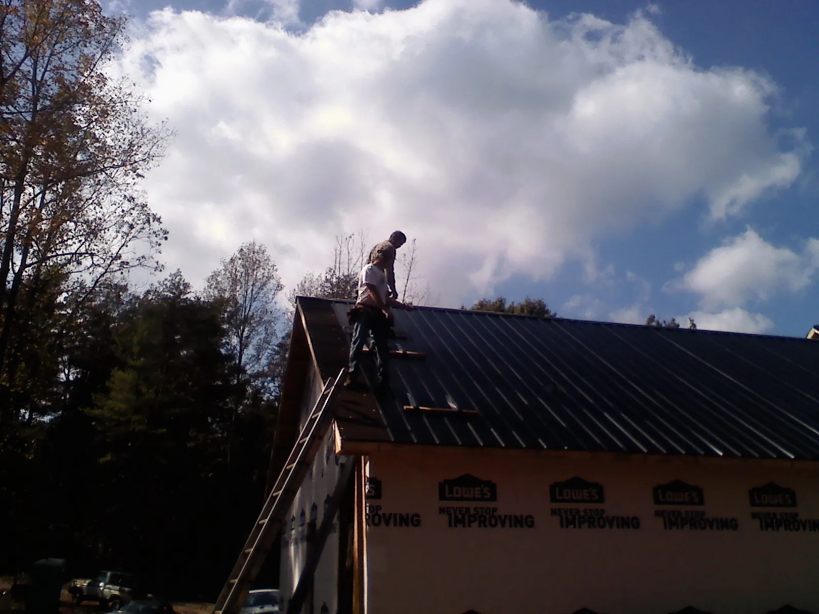 Roofer fastening dark metal panels high against a cloudy sky, from a Roof Inspection job in Hayesville