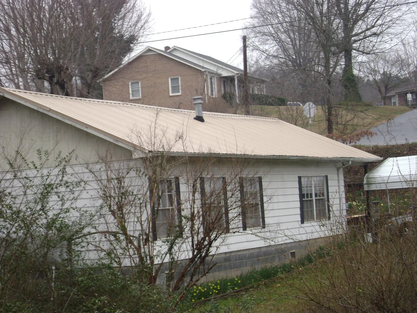 Tan metal roof on a white sided house set into a hillside — Commercial Roofing by Roofing Brothers in Hayesville