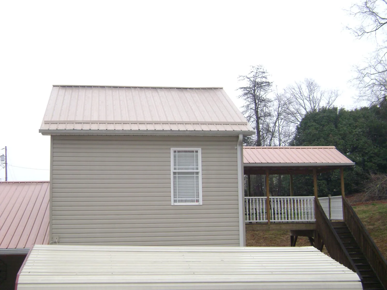 Tan metal roofs on a two story addition and attached porch, from a Roof Replacement job in Hayesville